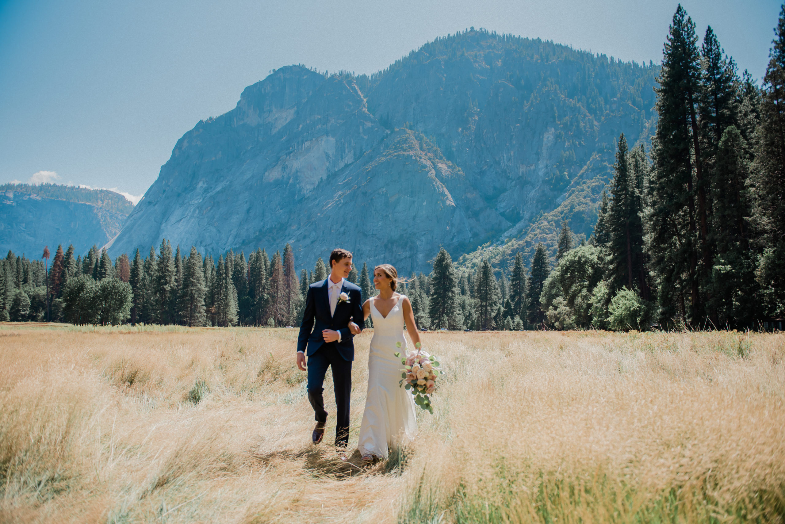 bride and groom walking in a meadow in yosemite and mountain in background